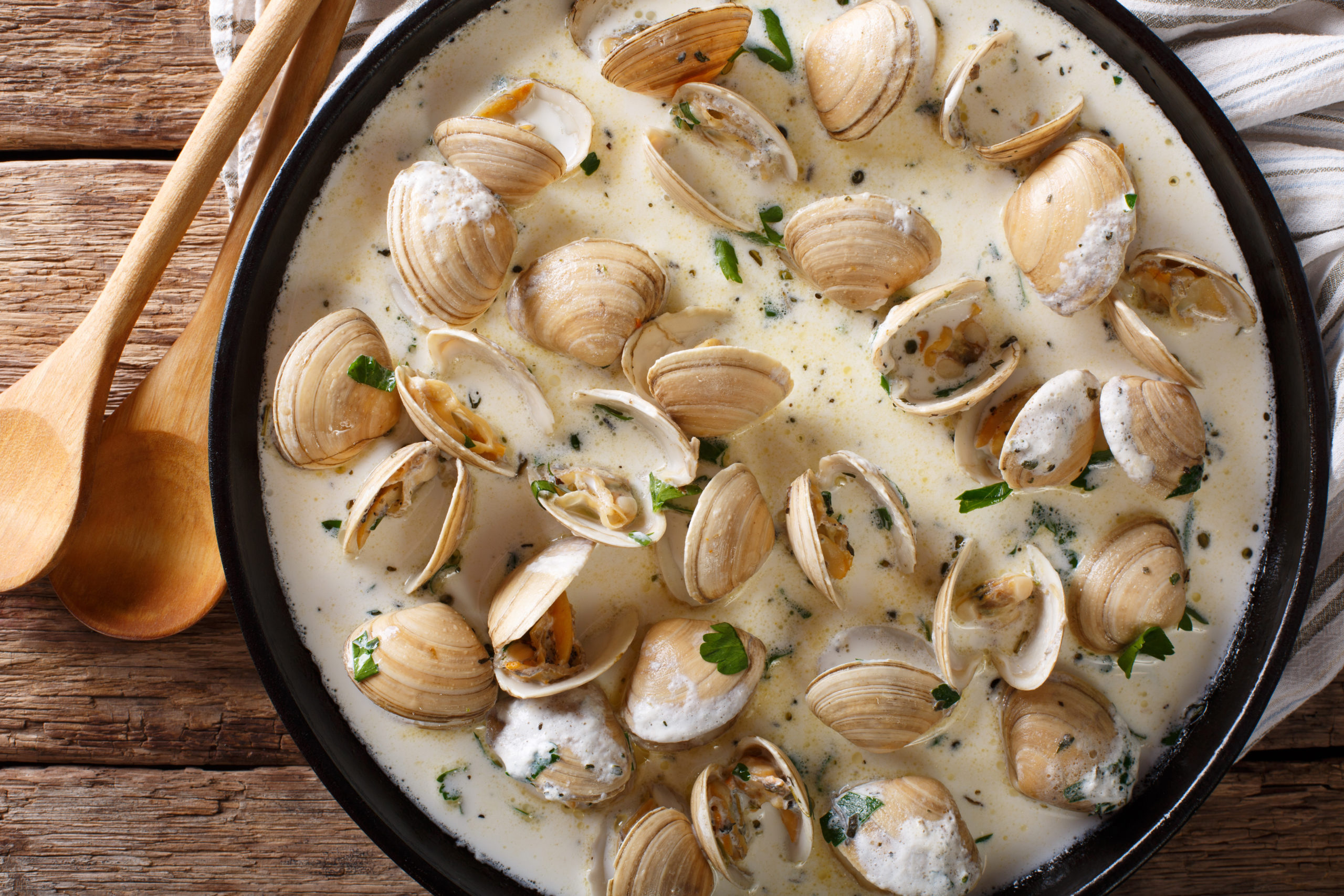 Tasty clams in a creamy sauce with garlic and greens close up on a table. horizontal top view